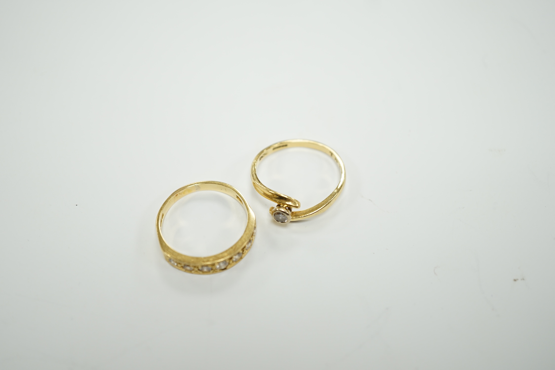 A modern 18ct gold and graduated seven stone diamond set half hoop ring, size O and a similar solitaire diamond ring with crossover setting, gross weight 6.4 grams.